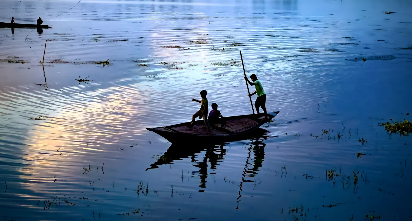 Blue hour: Two fishermen and a pole, mirrored in still water.